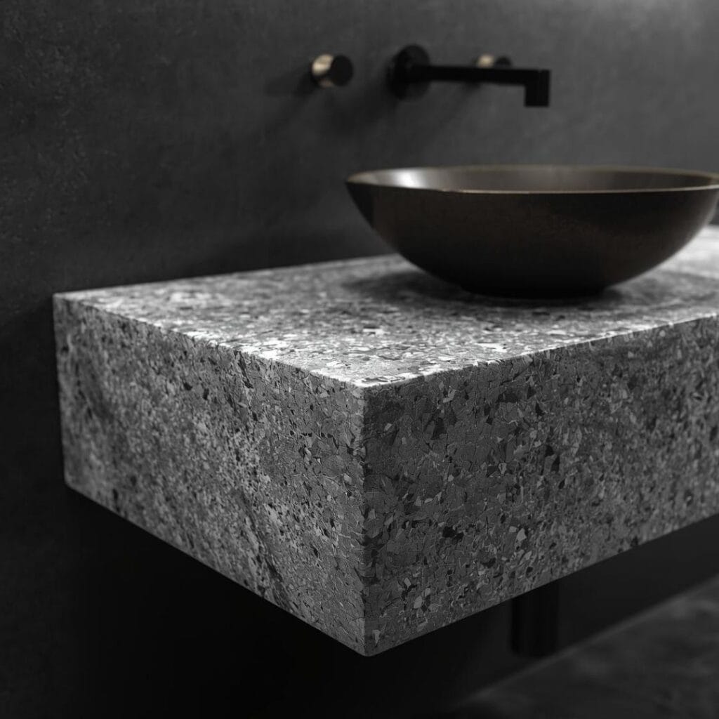 A close-up photograph of a contemporary bathroom vanity featuring a thick stone countertop and a modern chrome faucet.